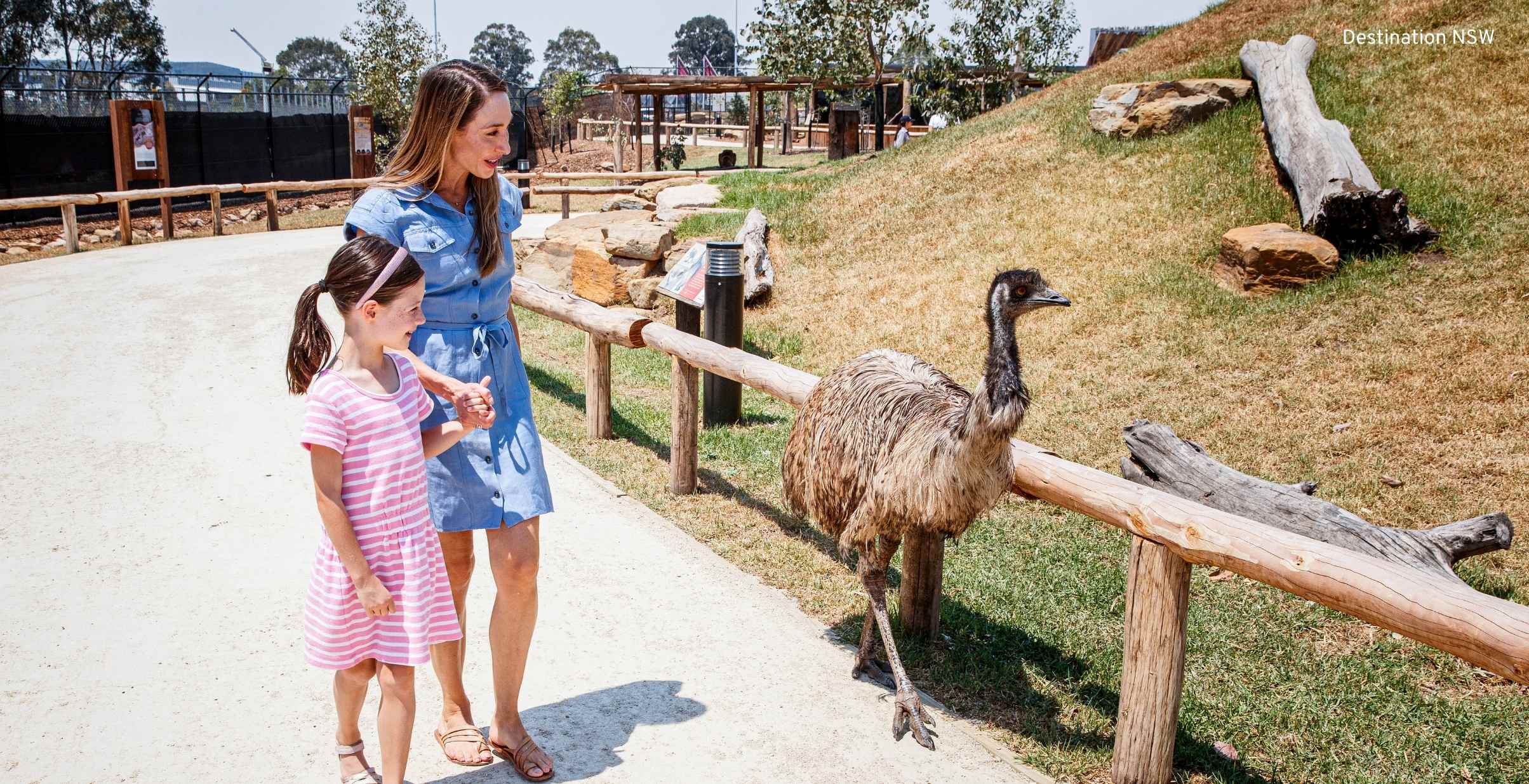Mother and daughter looking at wandering emu in wildlife park.