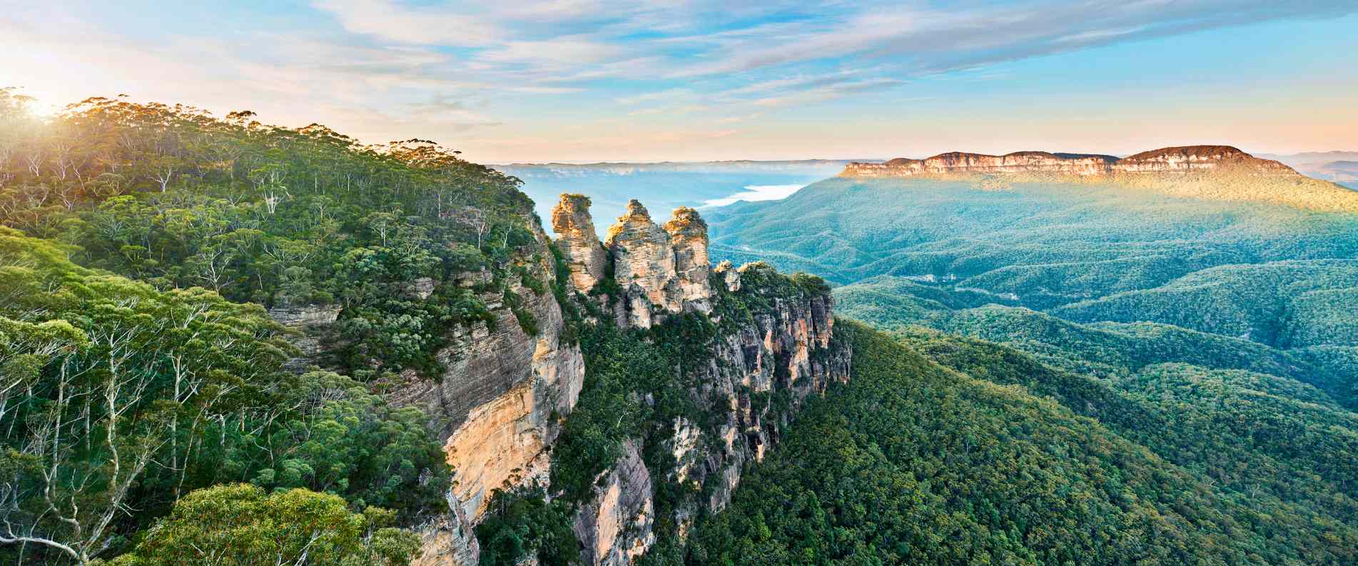 A scenic view of the iconic Three Sisters rock formation in the Blue Mountains, with rugged cliffs and a vibrant sky framing their distinctive shapes.