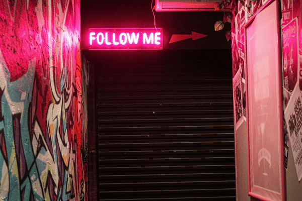 Neon pink light up sign that says follow me with stairs in the background